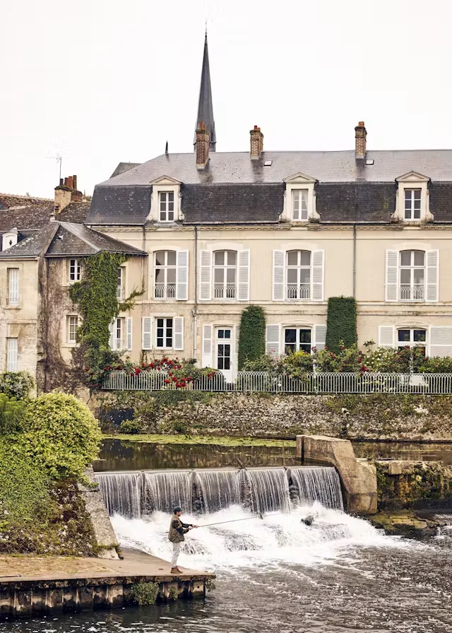 LVMH’nin Les Journées Particulières etkinliği kapsamında ziyaretçilere açılan ve lüks zanaat mirasını yansıtan tarihi Louis Vuitton L’Atelier Abbaye Vendôme’da, yemyeşil bitkilerle kaplı eski bir binanın arkasındaki manastırın sivri çan kulesi gökyüzüne uzanırken, önünden akan nehrin şelaleli kısmında bir adam sakin bir şekilde balık tutuyor.