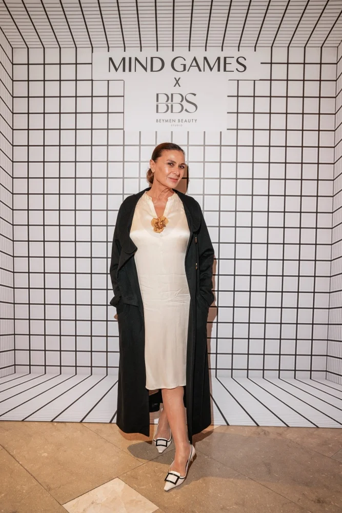 Oyuncu Hatice Aslan, zarif siyah bir bluz, dikkat çekici yuvarlak bir kolye ve doğal tonlarda bir makyajla, Mind Games Beymen Beauty Studio Oggusto davet etkinliğinde sıcak bir gülümsemeyle doğrudan kameraya bakarken görülüyor.