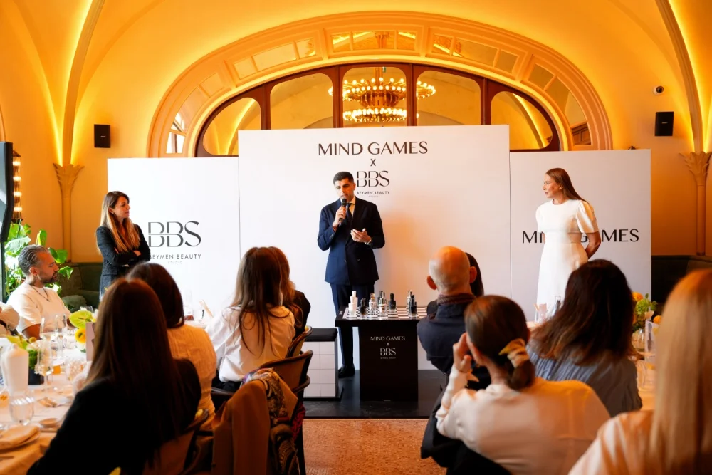 Mind Games Parfüm kurucusu Alex Shalbaf, aydınlık bir iç mekanda, düşünceli ve kendinden emin bir ifadeyle kameraya bakarken, markasının felsefesini yansıtan bu röportaj için sade ve şık bir giyimle poz veriyor.