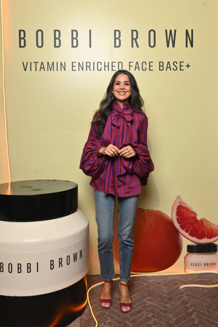 Bir kadın model, Bobbi Brown ürünleriyle yapılmış, pürüzsüz ve doğal duran makyajıyla kameraya hafifçe gülümsüyor; şeftali tonlarındaki allığı ve nude ruju, aydınlık göz makyajıyla uyumlu bir güzellik ve zarafet yansıtıyor, cilt tonu sağlıklı ve canlı görünüyor.