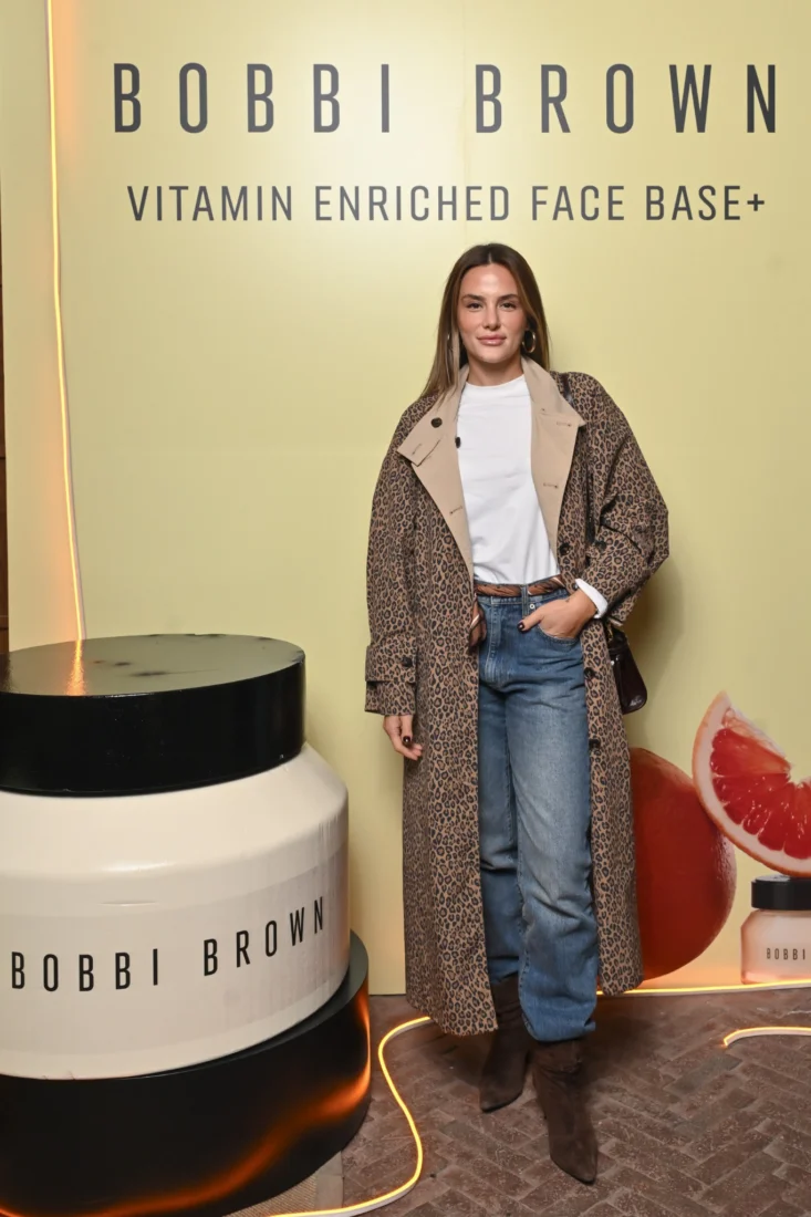 Ünlü makyaj sanatçısı Bobbi Brown, kameraya dönük hafif bir gülümsemeyle bakıyor, doğal güzelliğini vurgulayan zarif makyajı ve kısa saç kesimiyle aydınlık bir ortamda profesyonel bir duruş sergiliyor.
