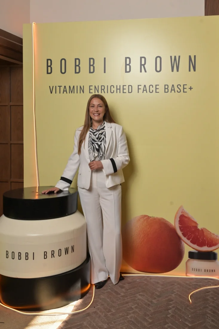 Yüzü yakın çekimdeki, doğal görünümlü makyajı ve geriye taranmış koyu renk saçlarıyla kameraya hafifçe gülümseyen zarif bir kadın, Bobbi Brown doğal makyaj felsefesinin modern güzelliğini vurguluyor.