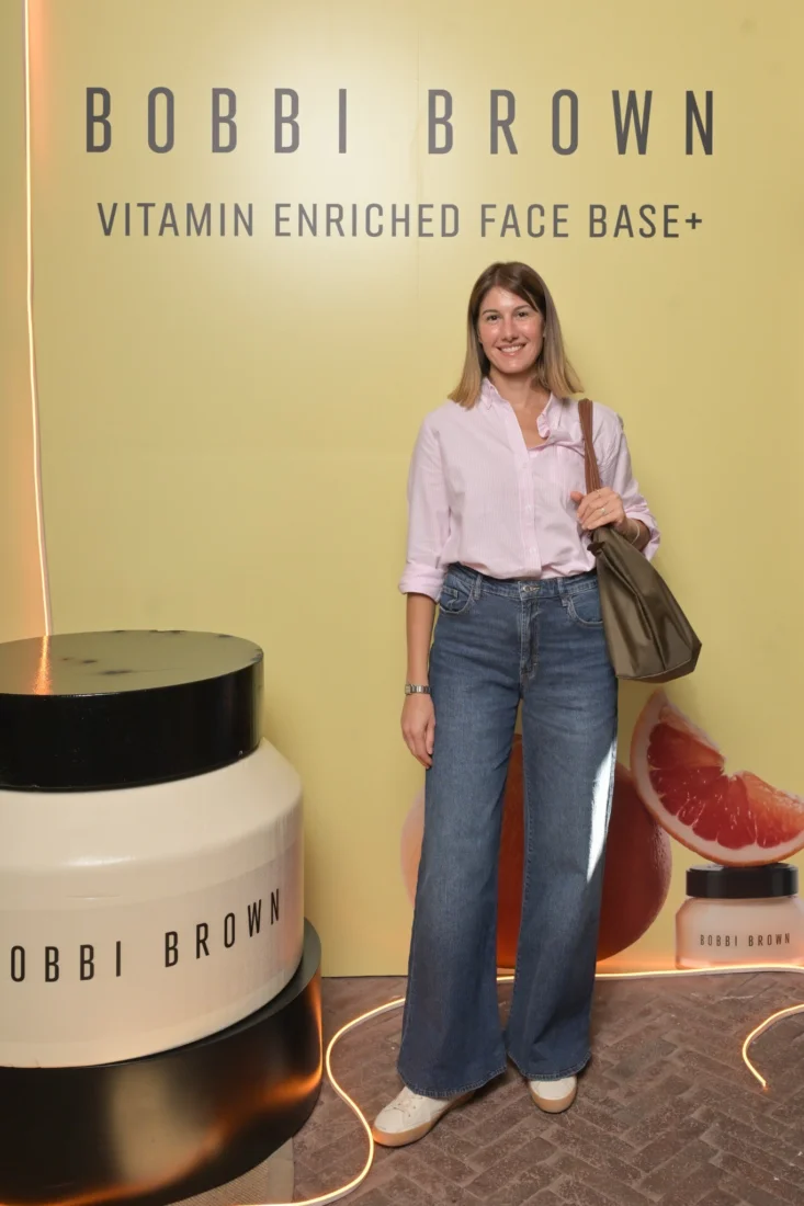 Makyaj gurusu Bobbi Brown, doğal güzelliği vurgulayan makyaj tekniklerini gösterirken, bir kişinin yüzüne hassasiyetle bir makyaj fırçası kullanarak özenli bir uygulama gerçekleştiriyor ve bu anı odaklanmış bir şekilde yansıtıyor.