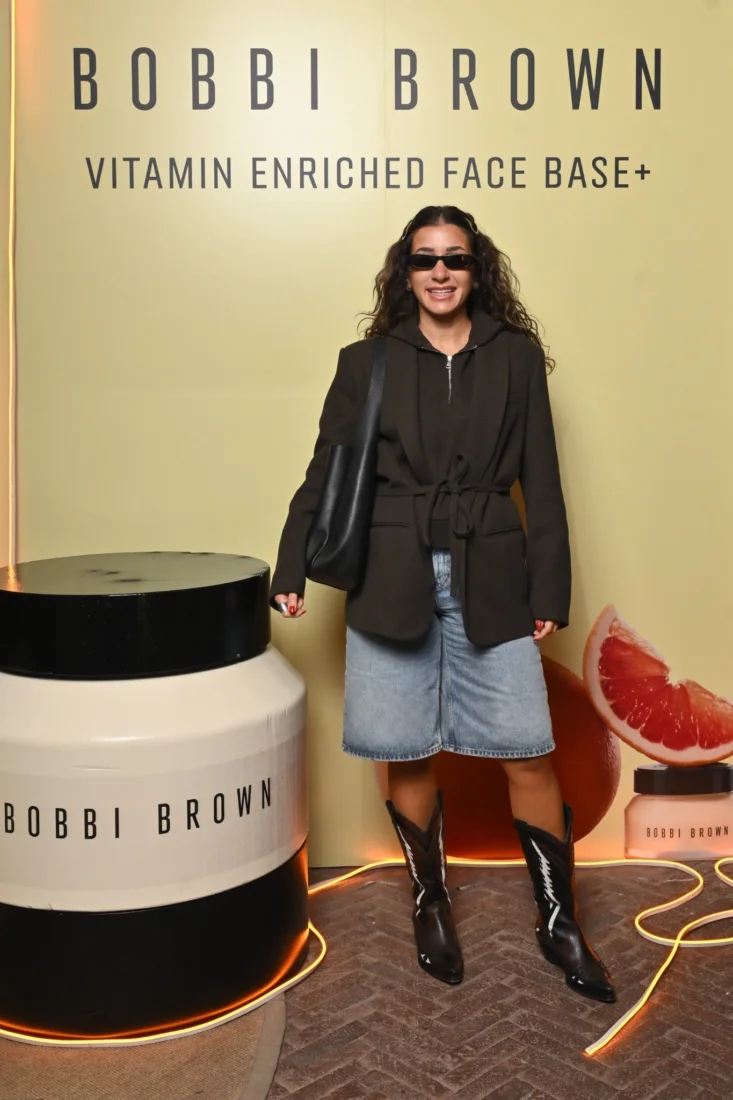 Şık ve modern bir mekanda gerçekleşen Bobbi Brown etkinliğinde bir araya gelen neşeli davetliler, keyifli sohbetler eşliğinde kameralara gülümserken, bir kadın elinde küçük siyah bir eşya tutarak, gecenin canlı ve enerjik atmosferini yansıtıyor.