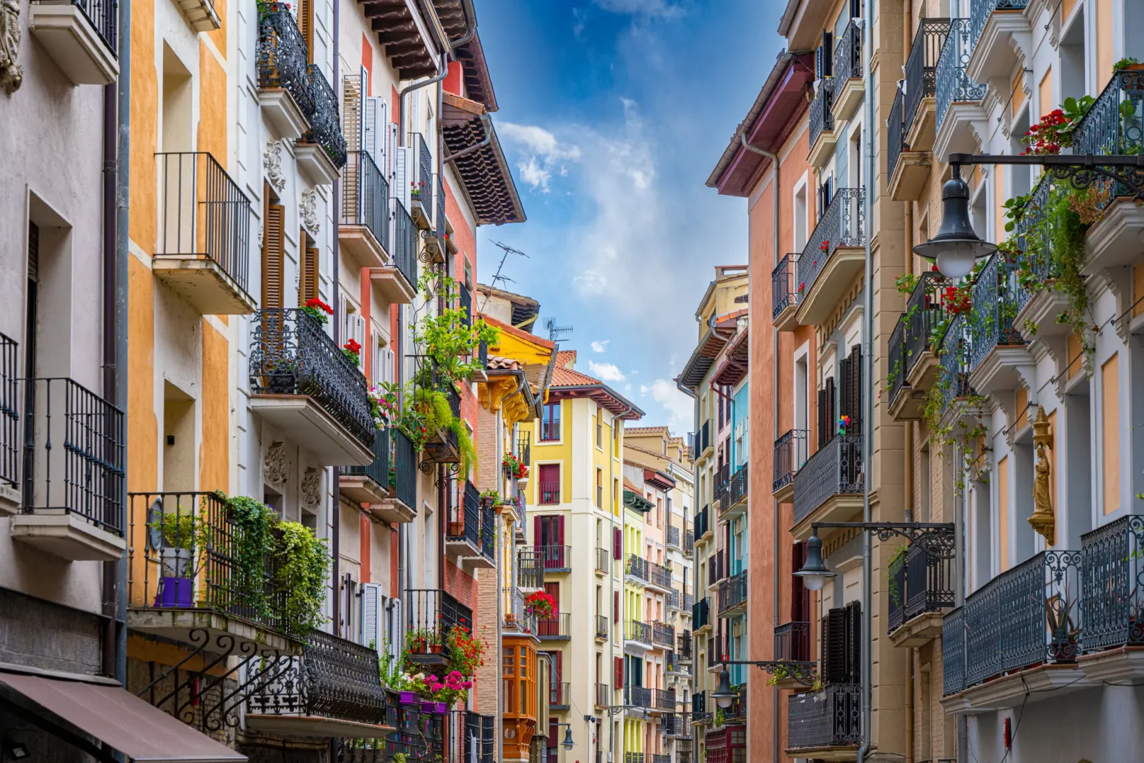 Pamplona'da, San Fermín Festivali'nin geleneksel boğa koşusu etkinliğinde, beyaz giysiler ve kırmızı fularlar içindeki kalabalık, tarihi taş sokaklarda coşkuyla ilerlerken, çevredeki eski binalar etkinliğin atmosferini tamamlıyor.