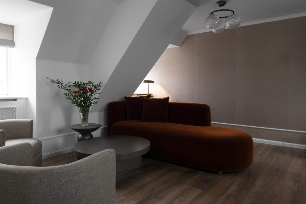 Park Lane Copenhagen'da, İskandinav şıklığını modern bir yorumla birleştiren bu rahat ve zarif otel odası, sıcak kahverengi kadife şezlongu, açık gri koltuk takımı, sade orta sehpası ve vazo içindeki kırmızı çiçeklerle sessiz lüks bir konaklama deneyimi sunuyor.