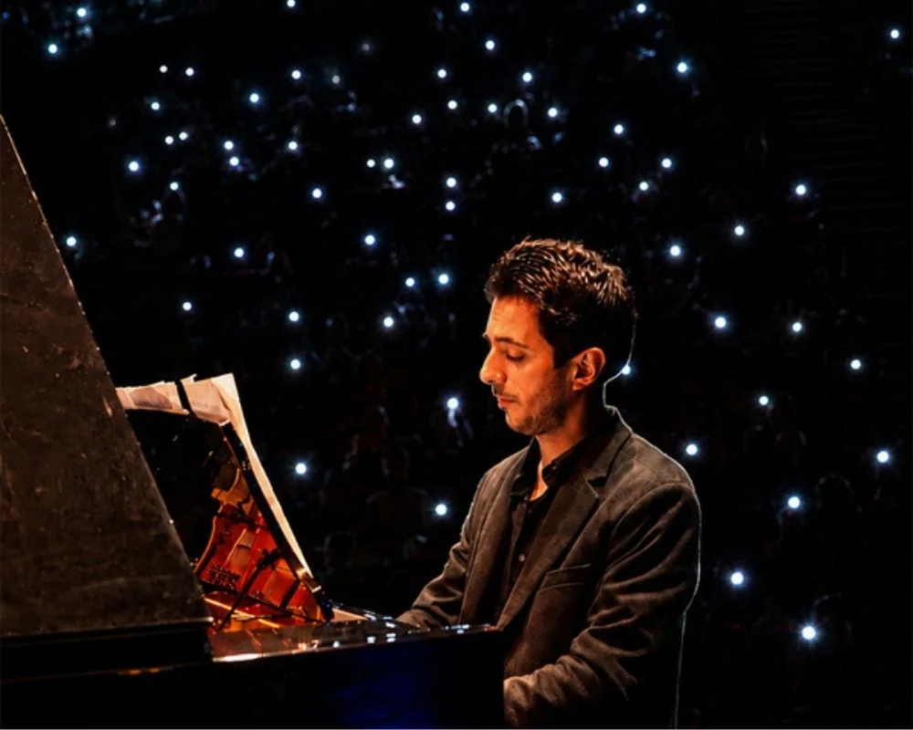 Piyanist Şamhal İsmail, karanlık ve modern bir konser sahnesinde piyano çalarken, kendisine yaylı çalgılar dörtlüsü eşlik ediyor; bu özel konser projesinde piyano ile iki keman, viyola ve çellonun birlikteliği dinleyicilere unutulmaz bir deneyim sunuyor.