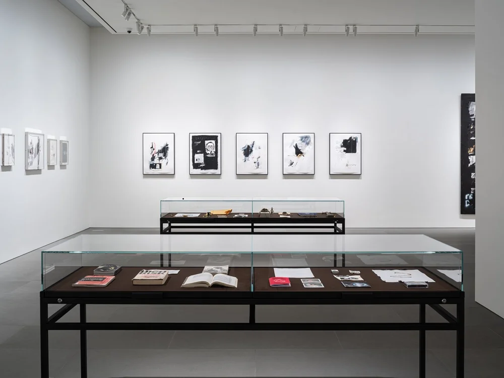 Seul Sanat Haftası'nın hareketli atmosferinde, aydınlık ve modern bir sanat galerisinde, sergilenen çağdaş eserlere dönük, etkinlik veya çalışmaları hakkında röportaj veren önemli bir figürün durağan ve düşünceli anı.
