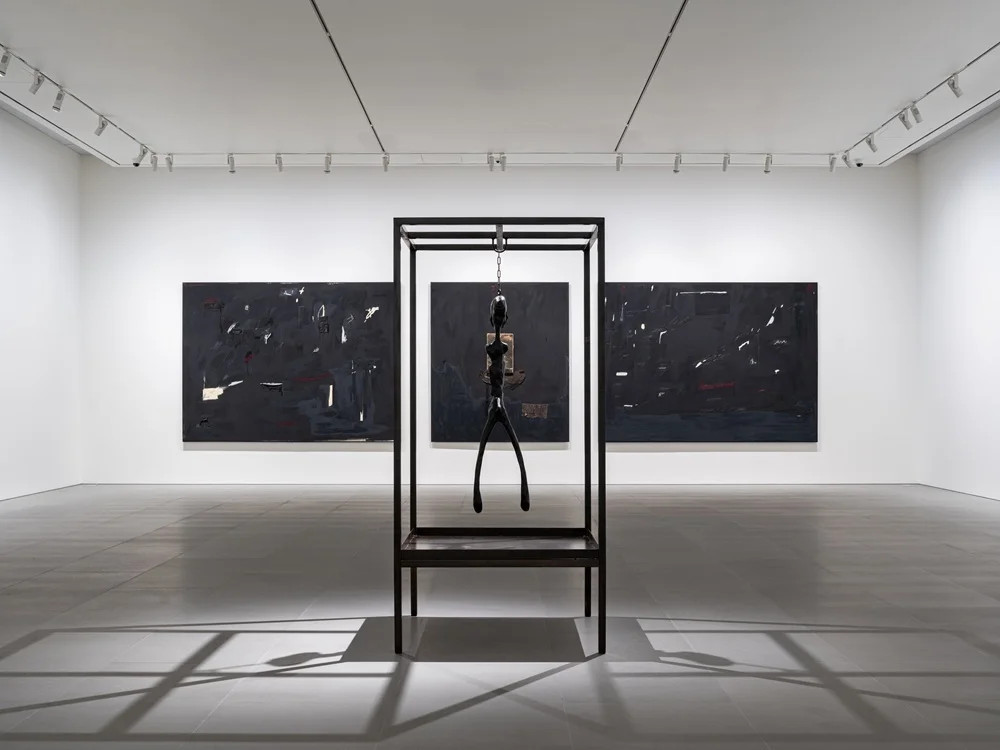 Geniş ve aydınlık bir sanat galerisinde, muhtemelen Seoul Sanat Haftası etkinlikleri kapsamında, bir muhabir büyük ve canlı renkli soyut bir tablonun yanında duran bir sanatçıyla samimi bir röportaj yaparken, arka planda diğer ziyaretçiler sessizce etrafı gözlemliyor.