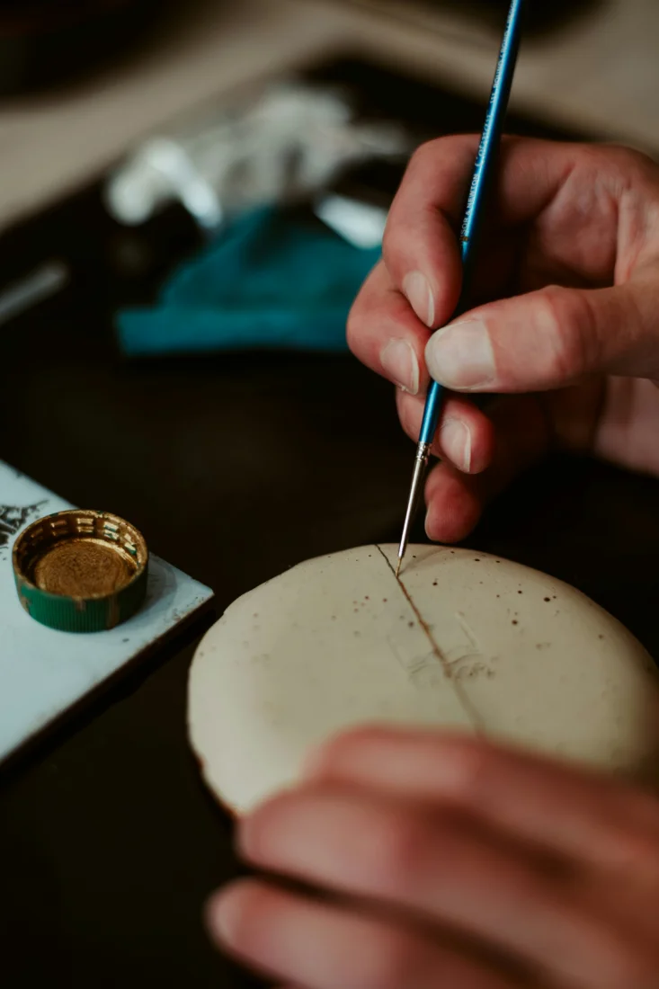 Tokyo'da skillcation rotasının bir parçası olarak kintsugi sanatının inceliklerini keşfeden bir yolculuğu simgeleyen, altın tozuyla onarılmış çatlakları belirgin, geçmişin izlerini taşıyan açık renkli bir seramik kâsenin yakın plan fotoğrafı.
