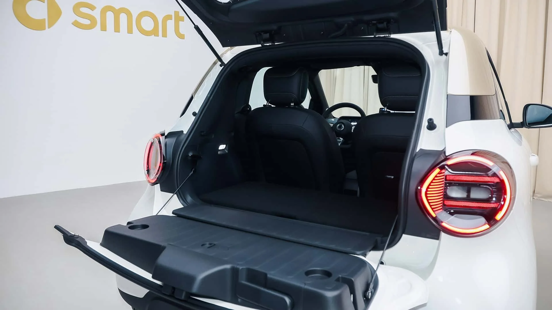 Modern tasarımlı Smart #2 2026 şehir içi elektrikli otomobilin parlak ışıklandırılmış bir alanda arka kısmından çekilmiş bu net görüntüsünde, geniş depolama alanı sunan açık bagajı ve kompakt yapısı dikkat çekiyor.