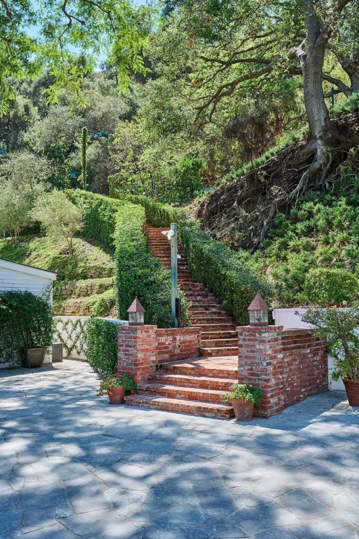 Taylor Swift’in eski Beverly Hills evinin bahçesinde ağaçların arasından yükselen kırmızı tuğla merdivenler
