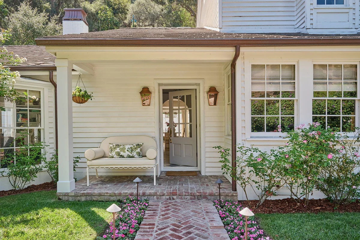 Beverly Hills’teki Pillsbury Estate’in beyaz ahşap cepheli girişi, tuğla yürüyüş yolu ve çiçekli veranda