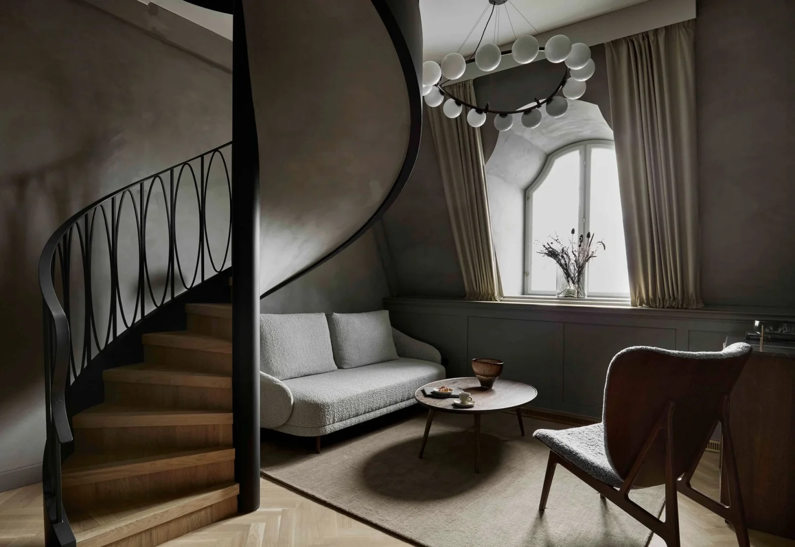 Villa Copenhagen'ın geniş ve modern lobi alanında, kavisli bej renkli bir kanepe ve koyu yeşil bir koltukla tamamlanan, bitkilerle süslenmiş ferah bir oturma düzeni, misafirlerine rahat ve şık bir karşılama sunuyor.