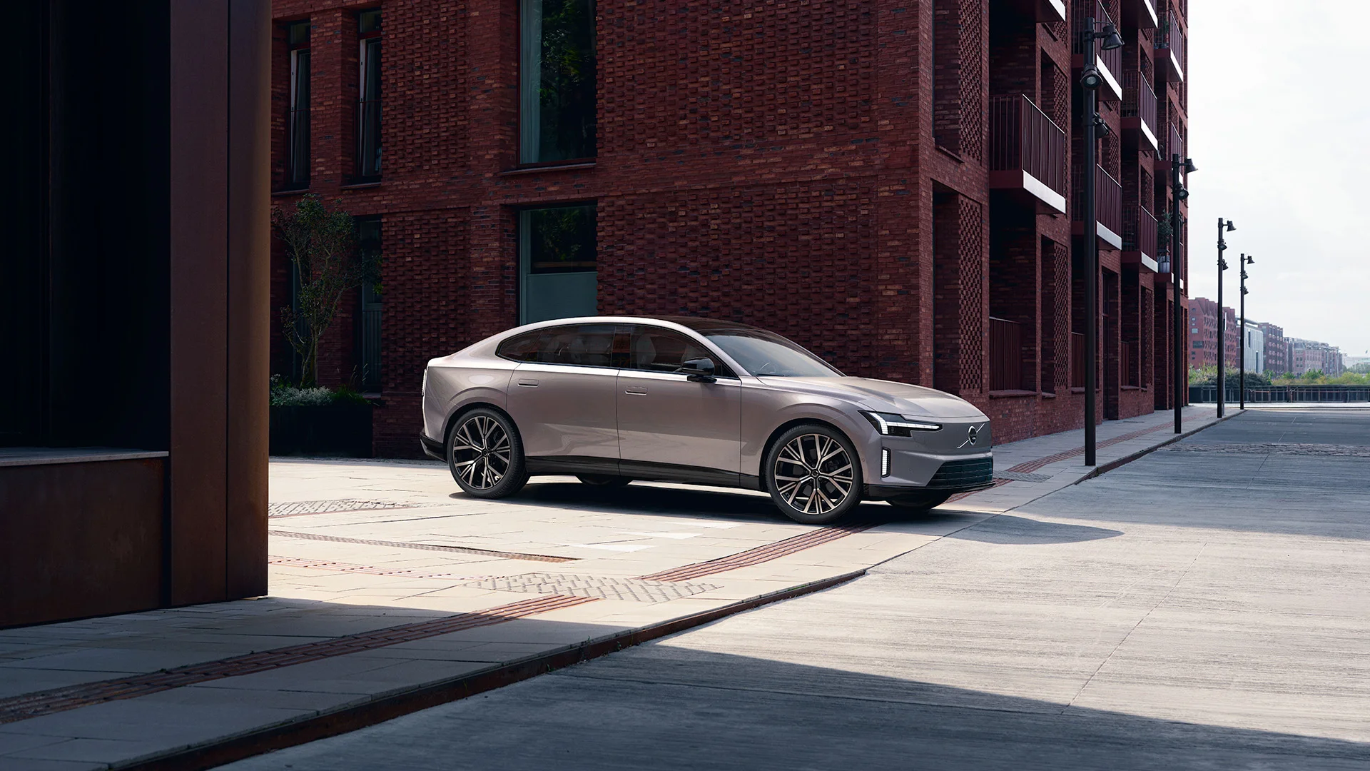 Ön planda, modern ve zarif hatlara sahip beyaz renkli bir Volvo ES90 elektrikli sedan otomobil, belirgin Thor's Hammer farları ve kapalı ön ızgarasındaki Volvo logosuyla lüks bir showroom ortamında veya stüdyoda park halinde, geleceğin elektrikli otomobil deneyimini yansıtan bir görünüm sergiliyor.